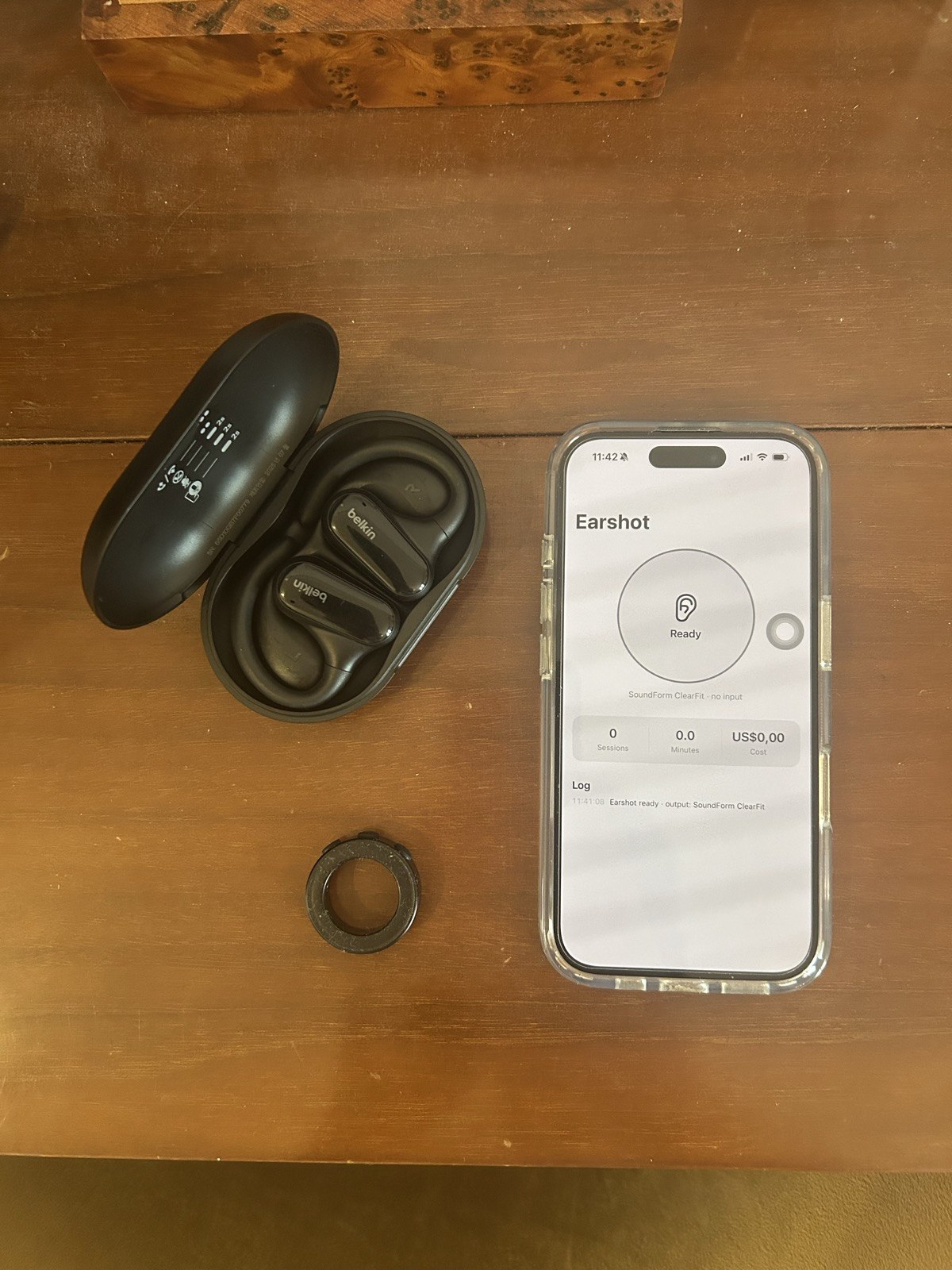 The kit on a wooden table: Belkin earbuds in their case, a Bluetooth ring, and an iPhone running Earshot.